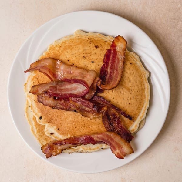 Golden pancakes topped with crispy bacon strips on a white plate.