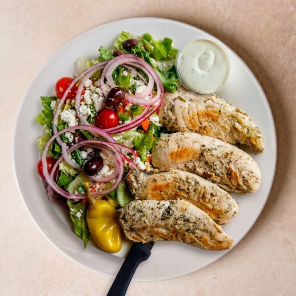 A plate of grilled chicken tenders with a side salad, feta, olives, red onion, and dressing.