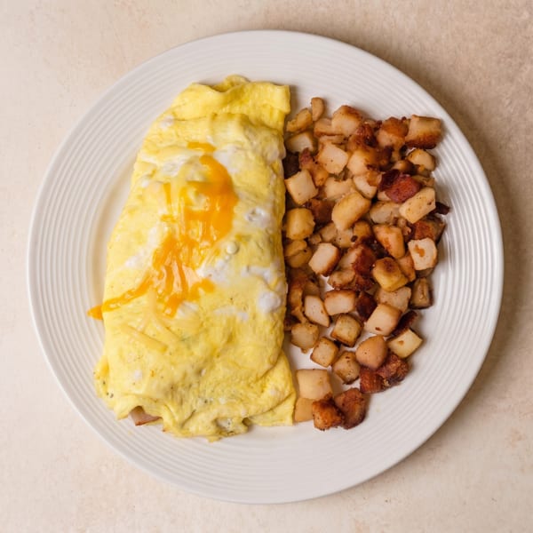 A cheese omelet with melted cheddar and white cheese, served with a side of crispy home fries.