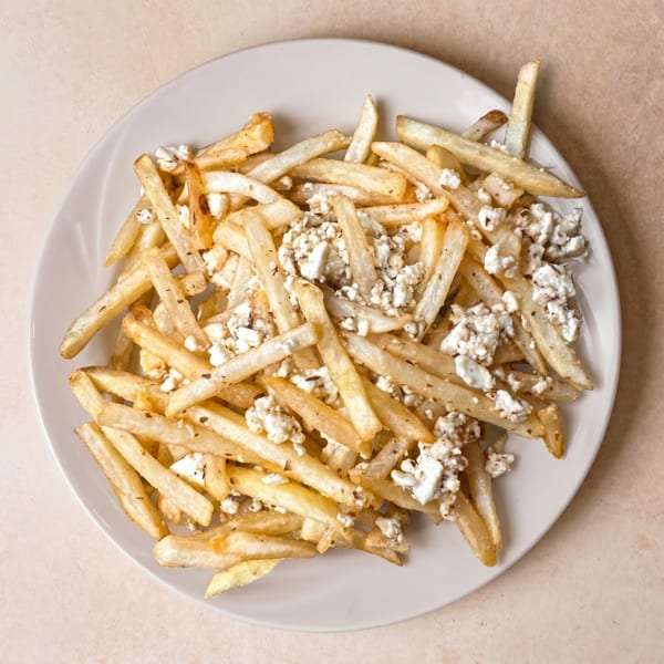 Golden french fries topped with crumbled white cheese and herbs on a white plate.